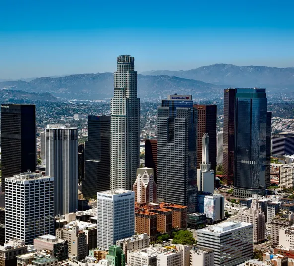 Downtown city skyline with tall skyscrapers and mountains in the background on a clear day.