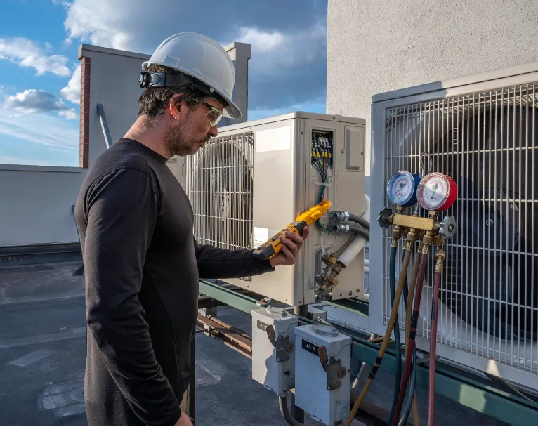 reliable-hvac-1 A technician in safety gear checks an HVAC unit with tools and gauges on a rooftop.
