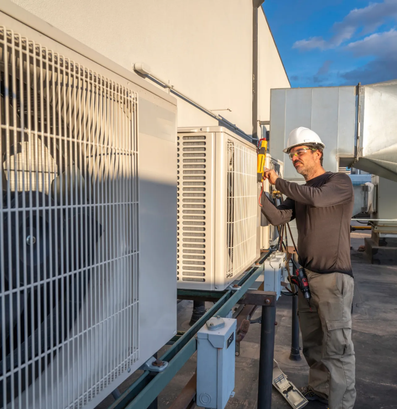 about-1 Technician in a hard hat servicing an outdoor air conditioning unit on a building rooftop.