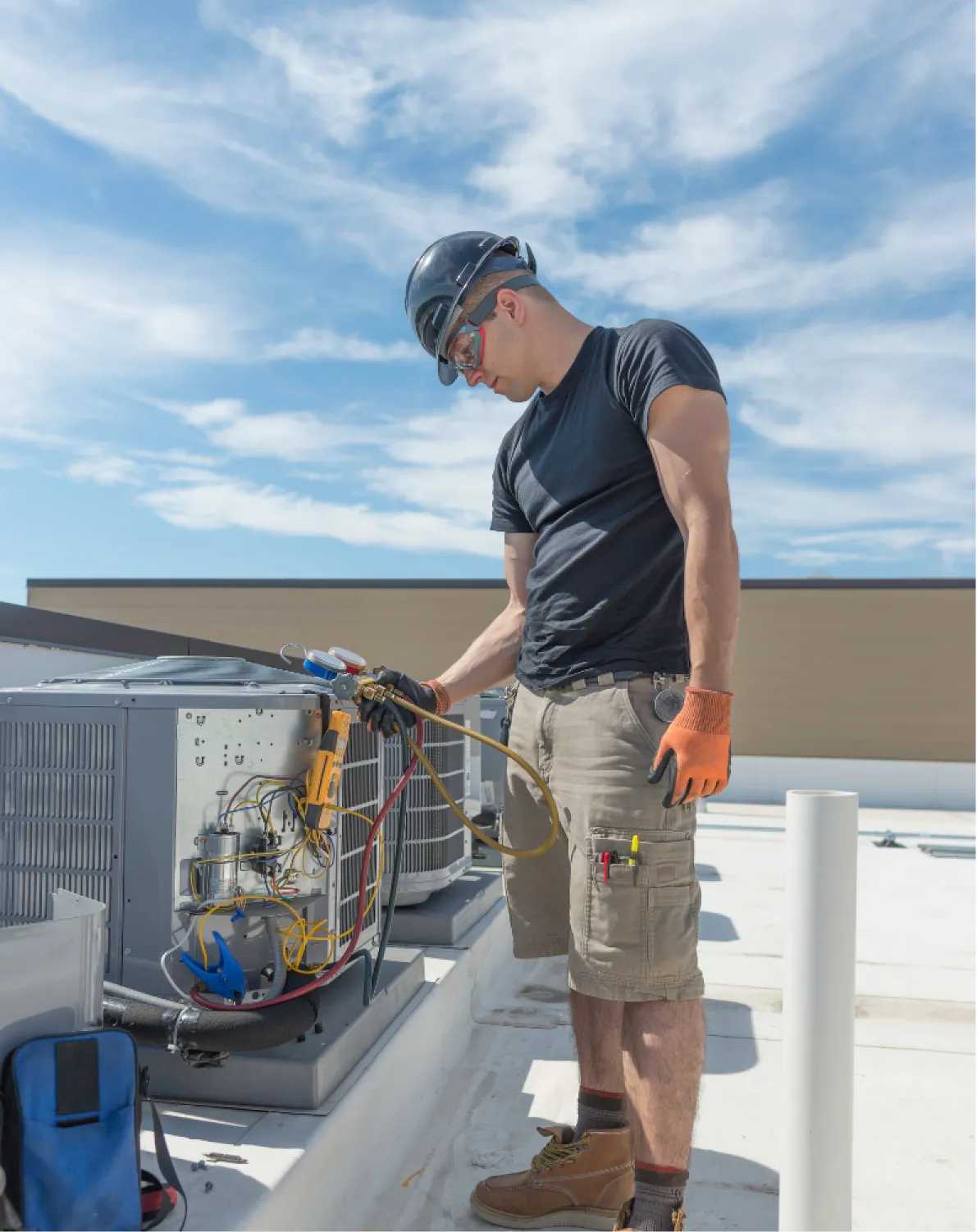 heating-repair-w A technician wearing safety gear repairs an HVAC unit on a rooftop under a clear blue sky.