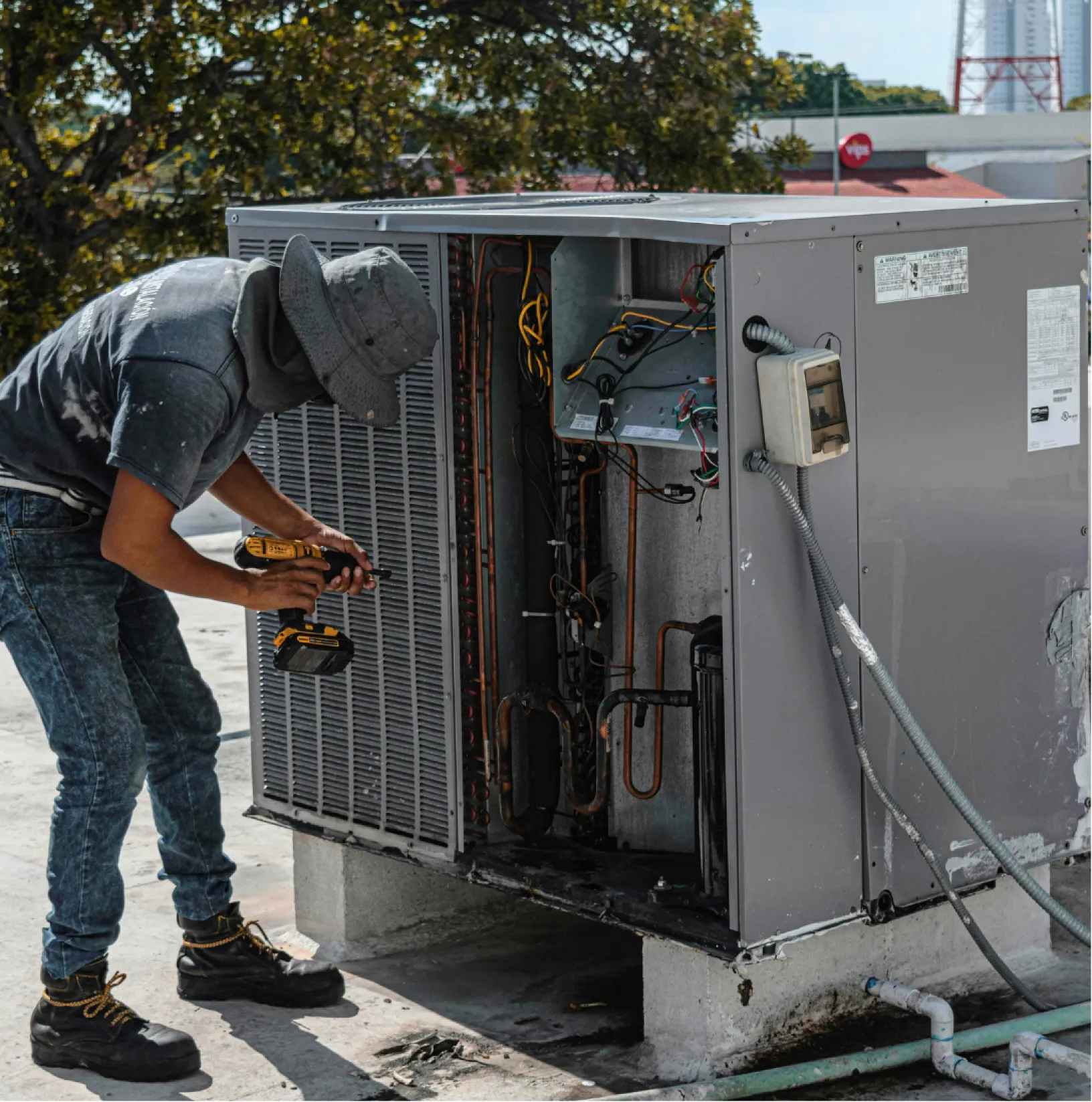 hvac-1 A technician repairs an outdoor HVAC unit with a power drill on a rooftop.