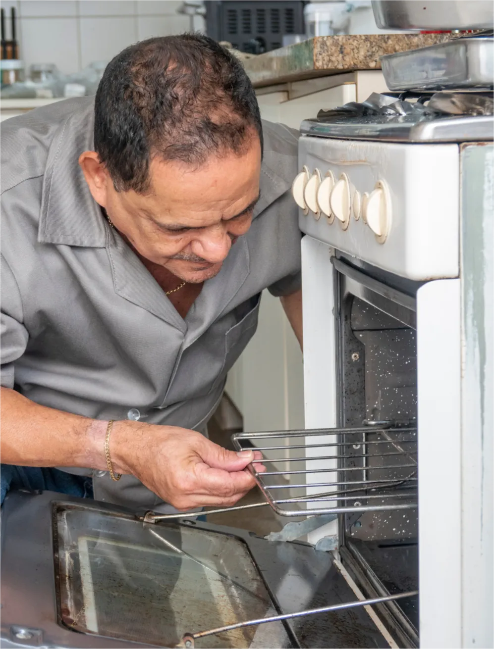Man in gray shirt installing an oven rack in a kitchen with the oven door open.
