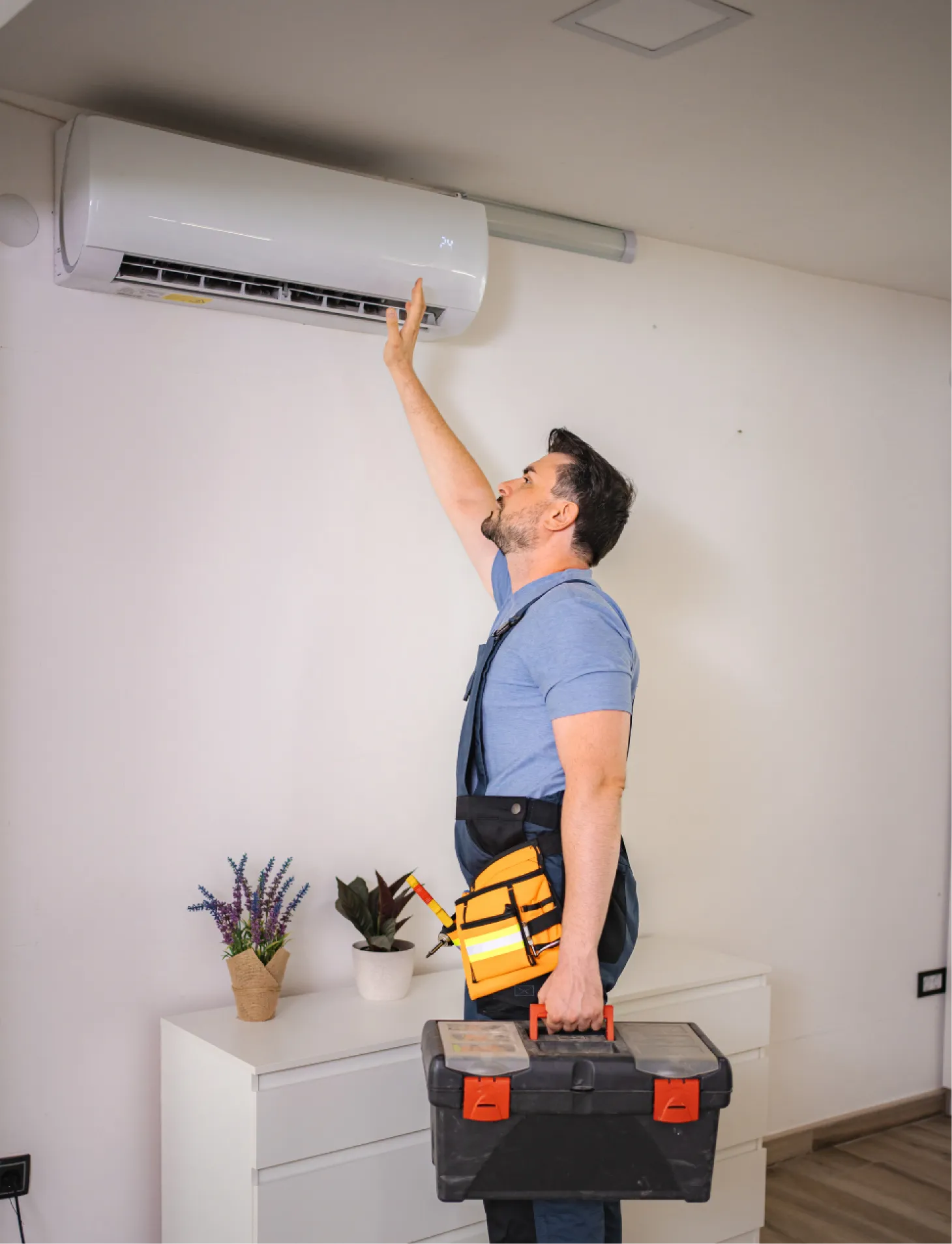 why-ac A technician inspects a wall-mounted air conditioner while holding a toolbox and a tool in his hand.