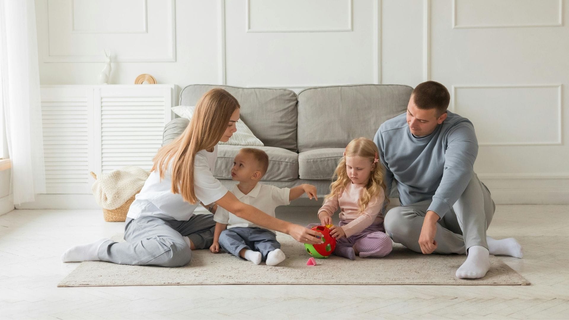 What Is a Zoned HVAC System A family of four sits on a rug, playing with a colorful toy together in a bright living room.