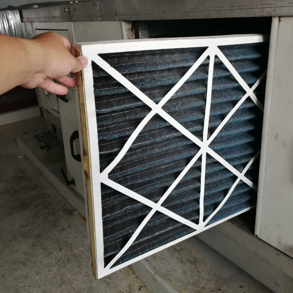 A hand removes a dirty air filter from an HVAC unit for replacement or cleaning.