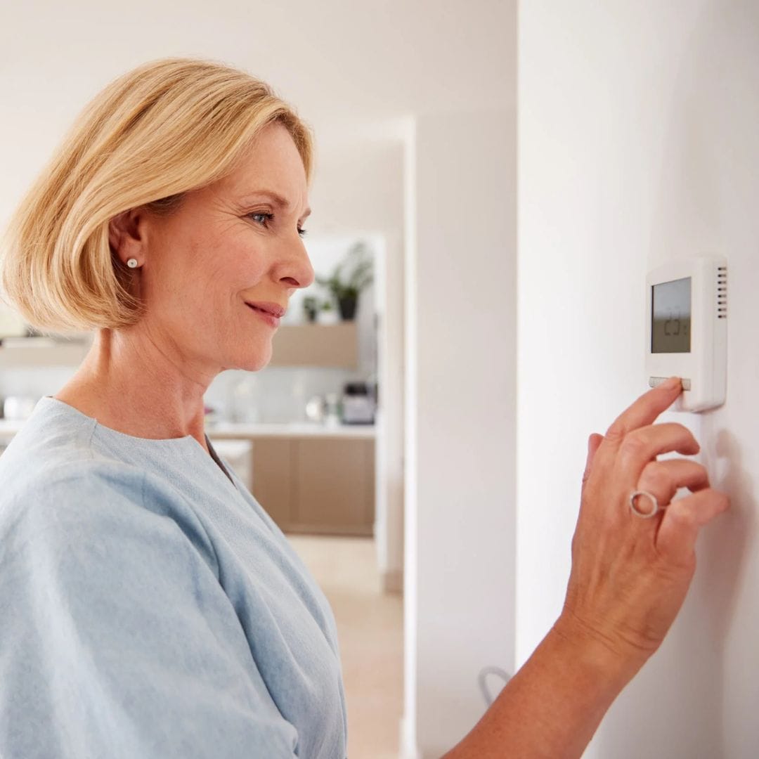 Woman adjusting a digital thermostat on a white wall in a bright, modern home.