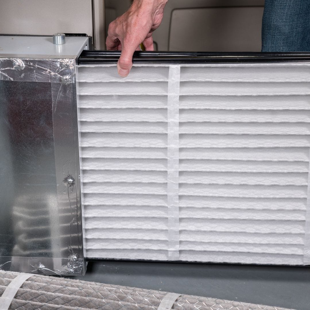 A person is performing HVAC maintenance Los Angeles style, installing or removing a white air filter from a metal HVAC unit.