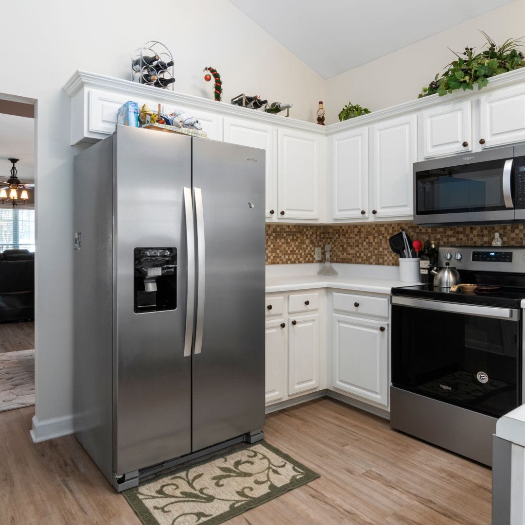 Modern kitchen with stainless steel fridge, white cabinets, tiled backsplash, and wood flooring.