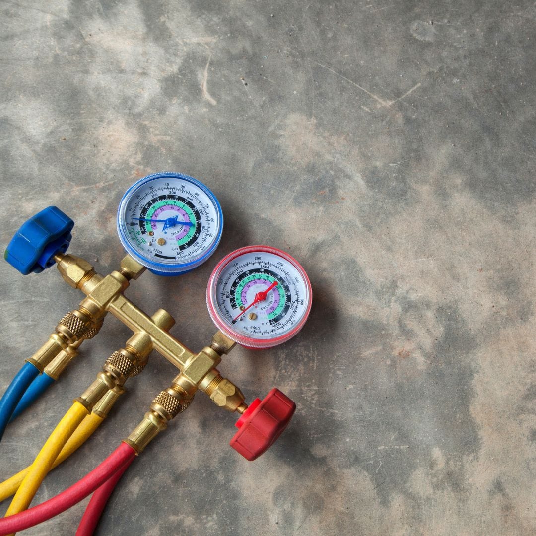 HVAC manifold gauge set with red, blue, and yellow hoses on a concrete surface.