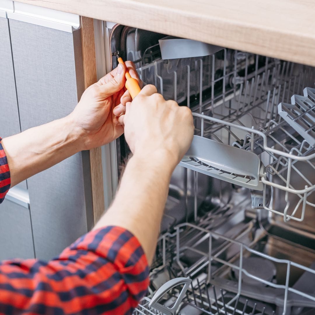 Person using a screwdriver to repair or adjust the inside of an open dishwasher.