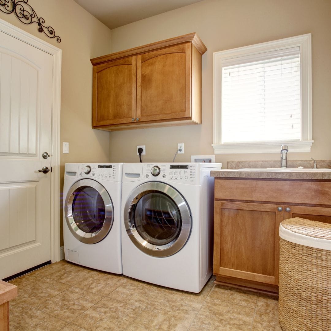 Laundry room with front-loading washer and dryer, wooden cabinets, sink, and wicker basket.