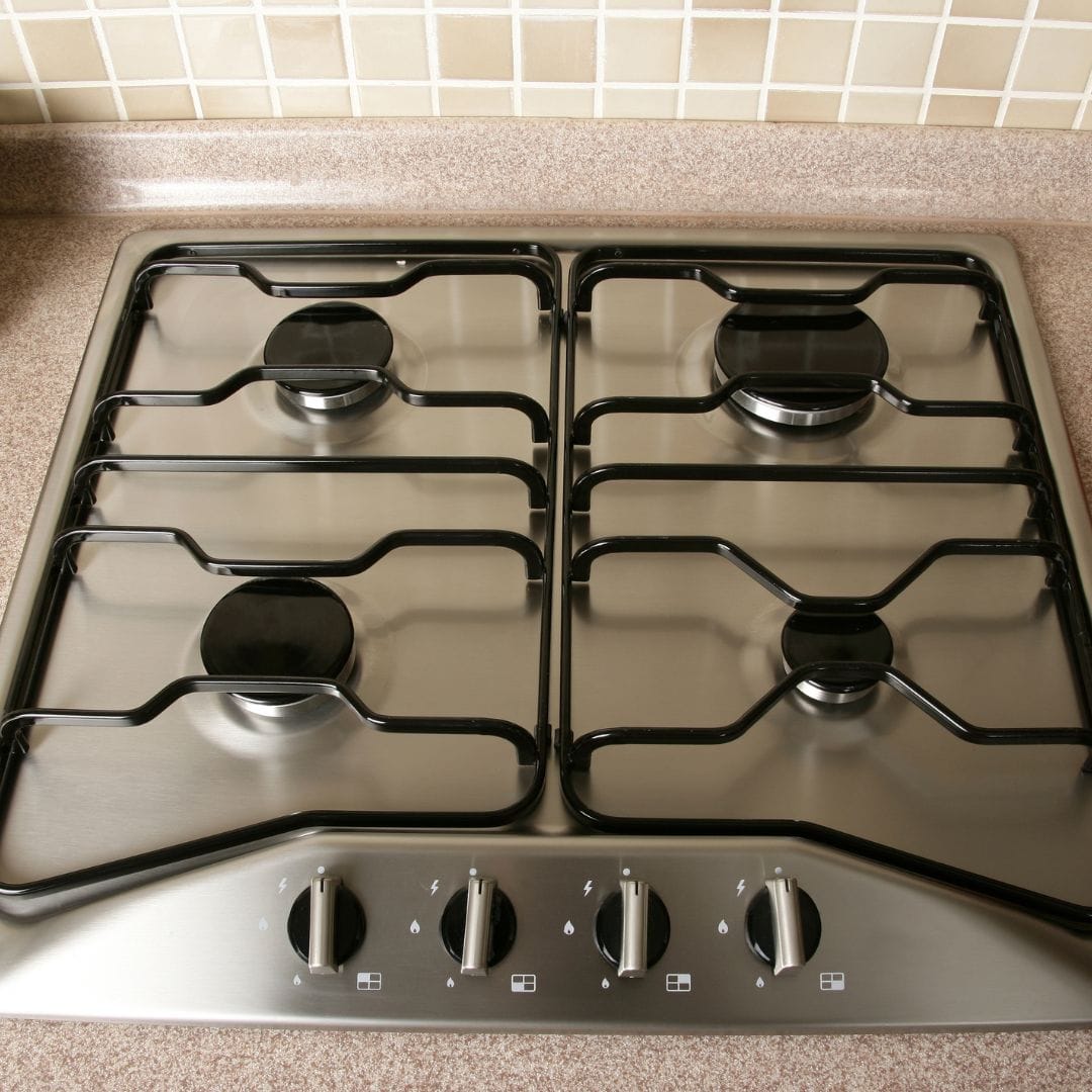 A stainless steel gas stove with four burners and control knobs, set into a speckled countertop.