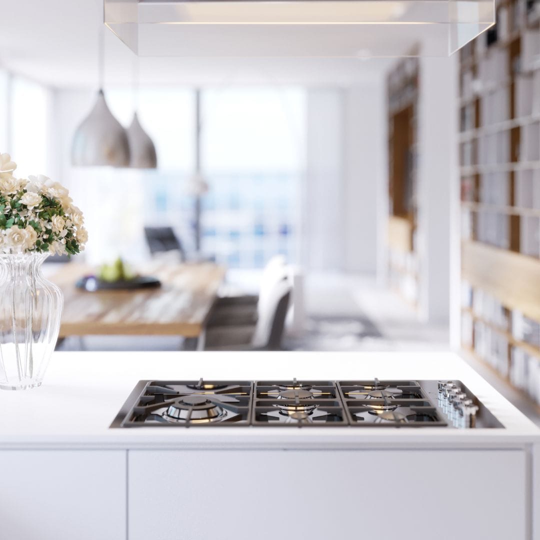 Modern kitchen with a gas stove, flowers in a vase, and a bright open dining area in the background.