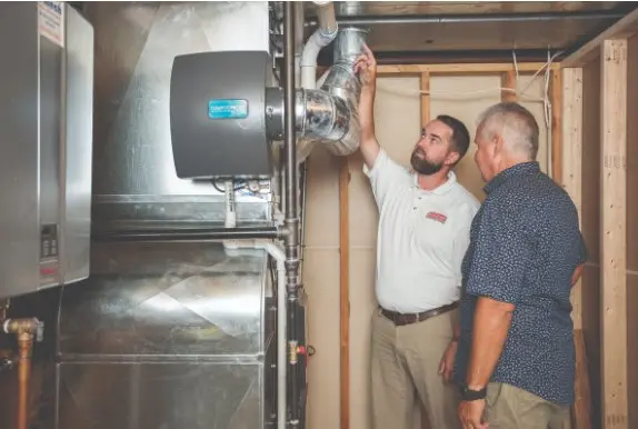 Canoga Park Tech w. Customer webp Two men inspect HVAC equipment and ductwork in an unfinished basement or utility room.